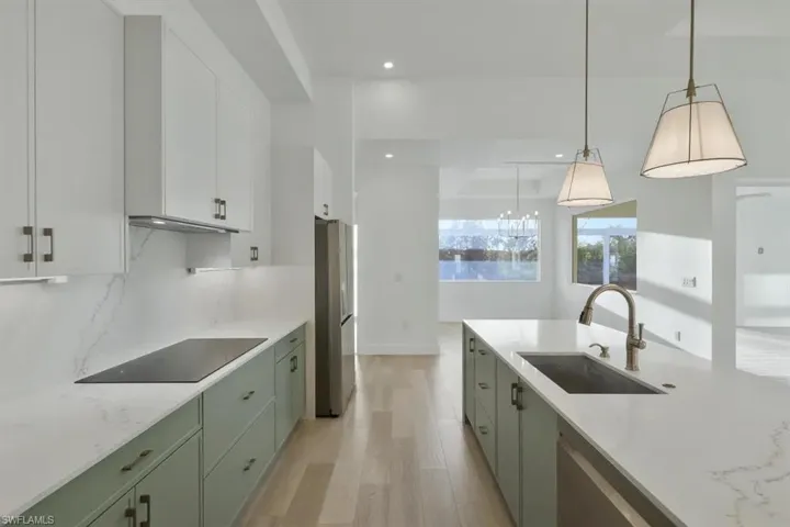Two tone kitchen with light stone countertops, light wood-style flooring, stainless steel appliances, pendant lighting, and backsplash