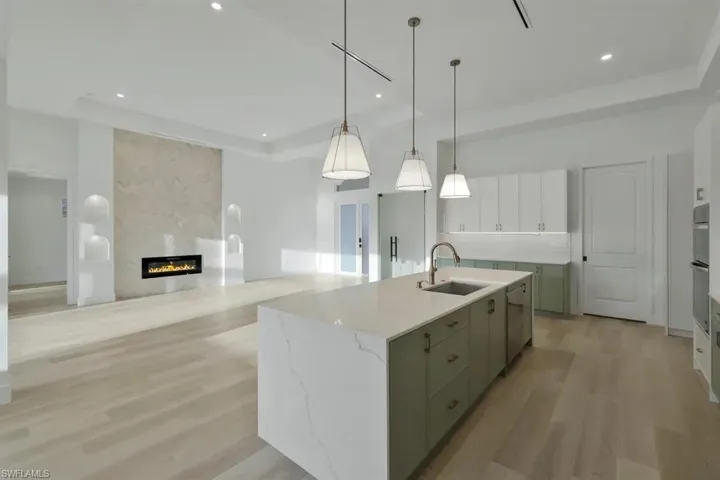 Dual tone kitchen featuring two tone color scheme, a kitchen island with sink, light wood-type flooring, light stone countertops, and a large fireplace
