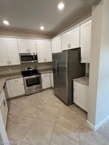 Kitchen with stove, white cabinetry, stainless steel fridge, light stone countertops, and recessed lighting