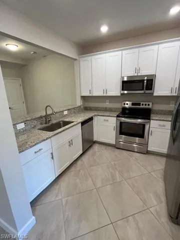 Kitchen featuring white cabinetry, stove, light stone countertops, fridge, and dishwasher