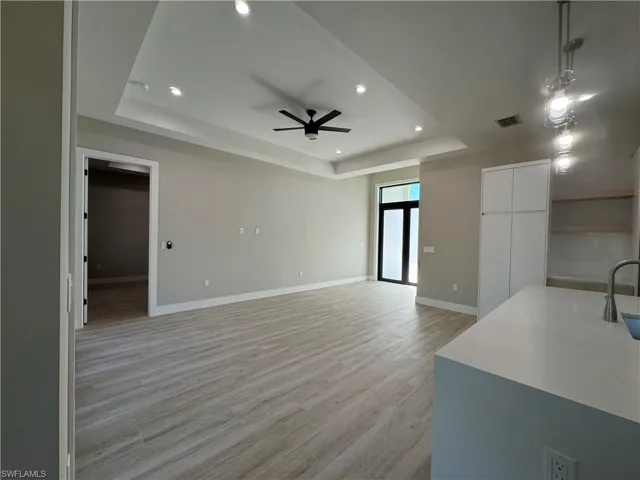 Unfurnished living room featuring a ceiling fan, light recessed lighting, and a tray ceiling