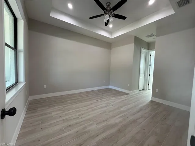 Unfurnished room featuring ceiling fan, light wood-style floors, recessed lighting, and a tray ceiling