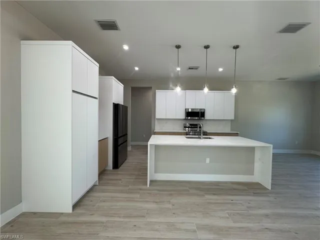 Kitchen featuring pendant lighting, a kitchen island with sink, white cabinetry, and modern cabinets