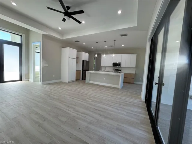 Kitchen featuring open floor plan, white cabinets, a center island with sink, hanging light fixtures, and a tray ceiling