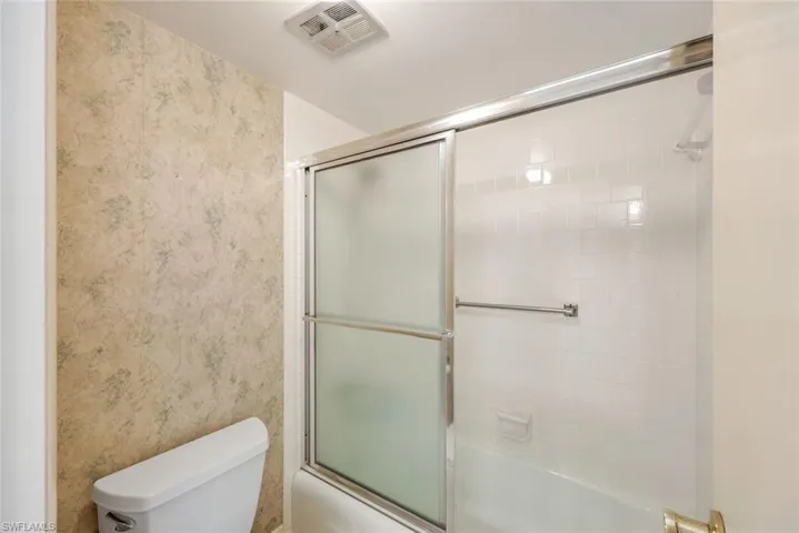 Bathroom featuring enclosed tub / shower combo and wallpapered walls