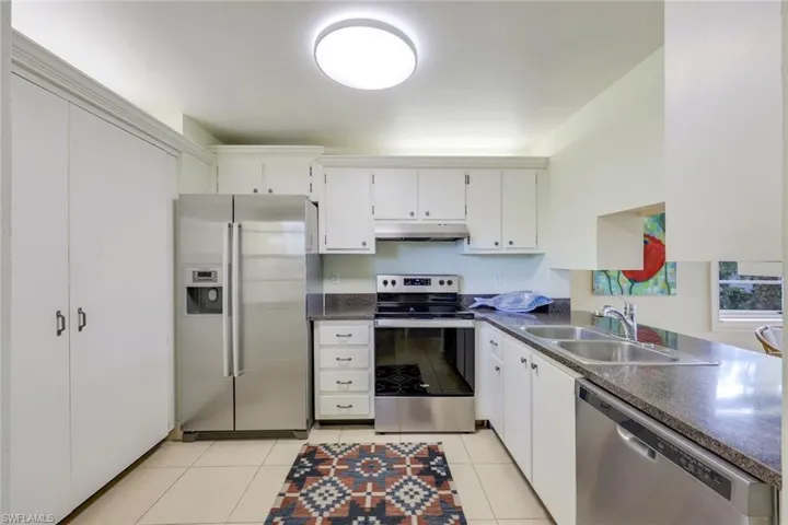 Kitchen with stainless steel appliances, dark countertops, white cabinetry, and light tile patterned flooring