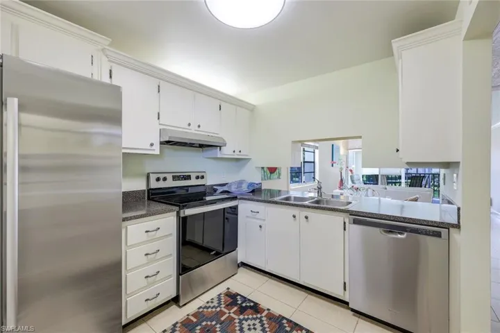 Kitchen with stainless steel appliances, white cabinetry, dark countertops, and light tile patterned floors