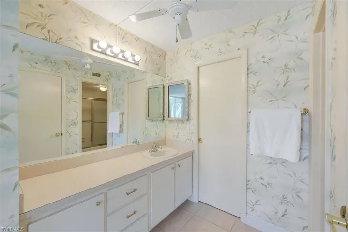 Full bath with vanity, light tile patterned flooring, wallpapered walls, ceiling fan, and a textured ceiling