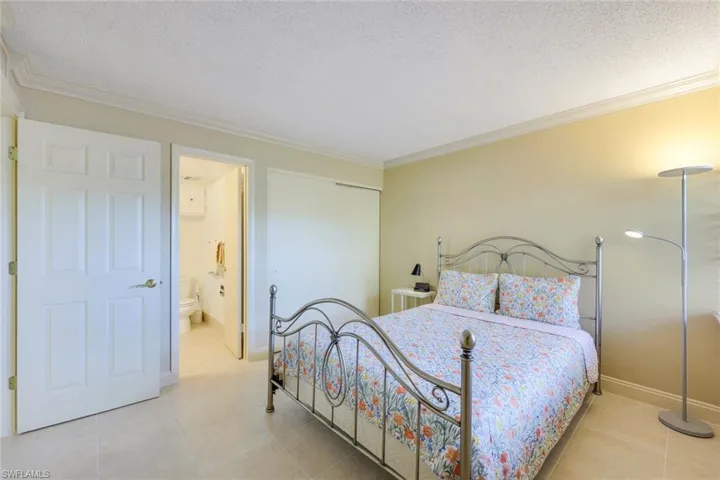 Bedroom with crown molding, a textured ceiling, a closet, ensuite bathroom, and light tile patterned floors