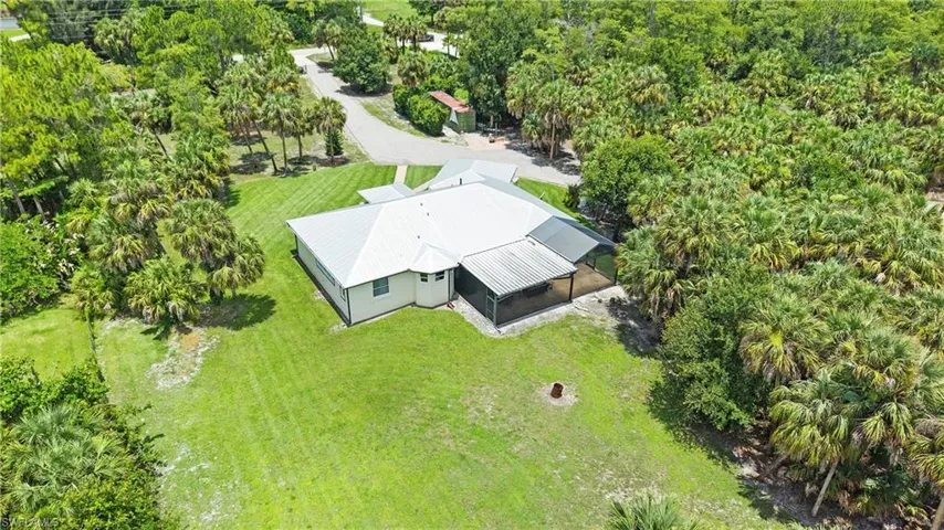 Expansive grounds featuring a manicured lawn, abundant mature palm trees, and a screened outdoor living area