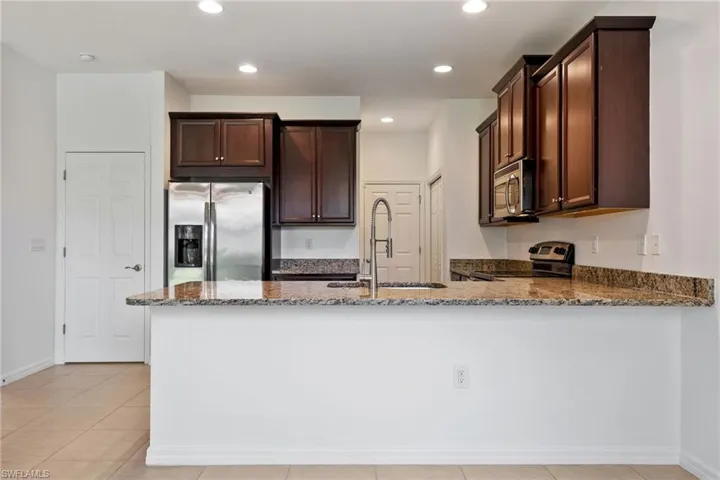 Kitchen featuring appliances with stainless steel finishes, stone counters, dark brown cabinets, a peninsula, and recessed lighting
