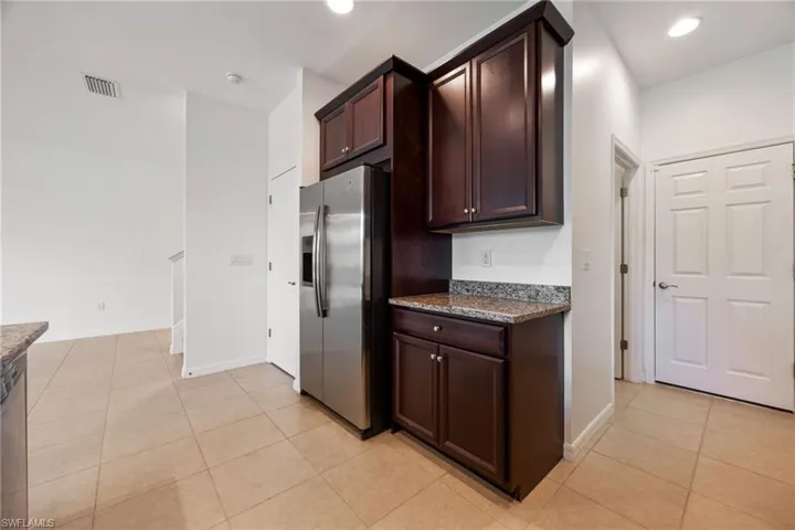 Kitchen with stainless steel fridge, light tile patterned floors, dark stone countertops, dark brown cabinets, and recessed lighting