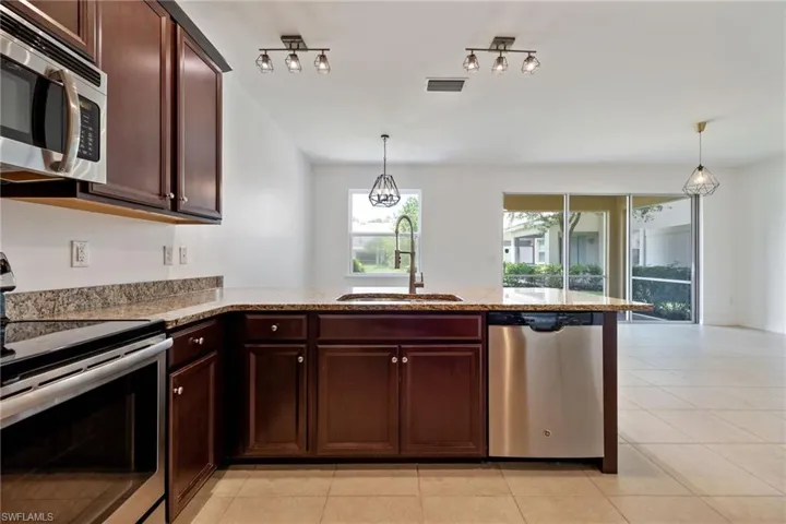 Kitchen with appliances with stainless steel finishes, a peninsula, light stone countertops, and hanging light fixtures
