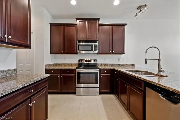 Kitchen with appliances with stainless steel finishes, light stone counters, light tile patterned floors, and recessed lighting