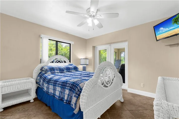Tiled bedroom with multiple windows, french doors, and ceiling fan