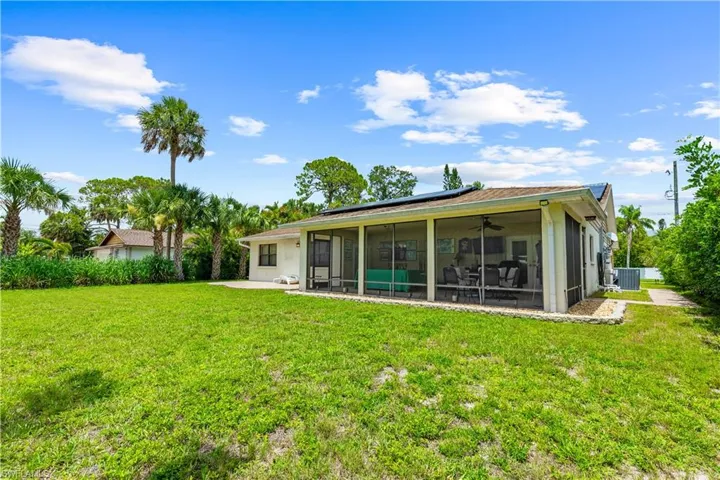 Rear view of house featuring a sunroom, solar panels, ceiling fan, a yard, and a patio