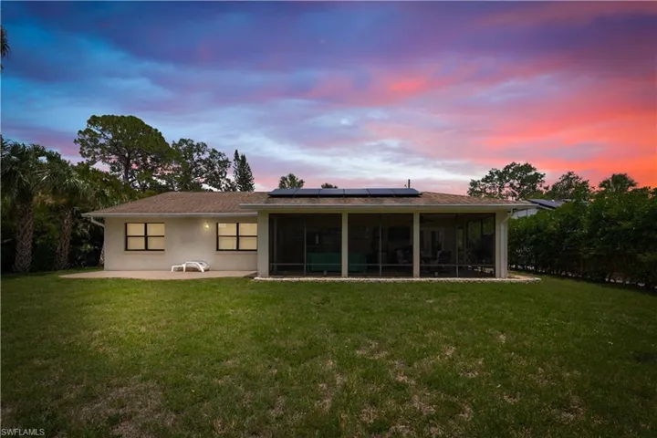 Rear view of house with solar panels, a sunroom, a lawn, and stucco siding