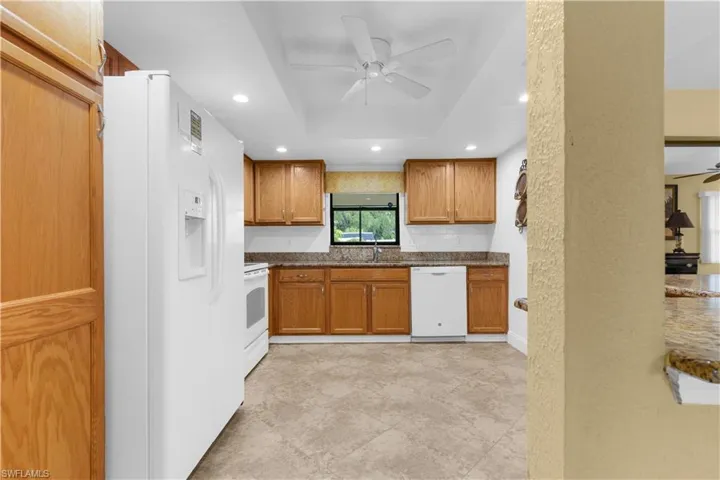 Kitchen featuring white appliances, ceiling fan, a raised ceiling, brown cabinetry, and recessed lighting
