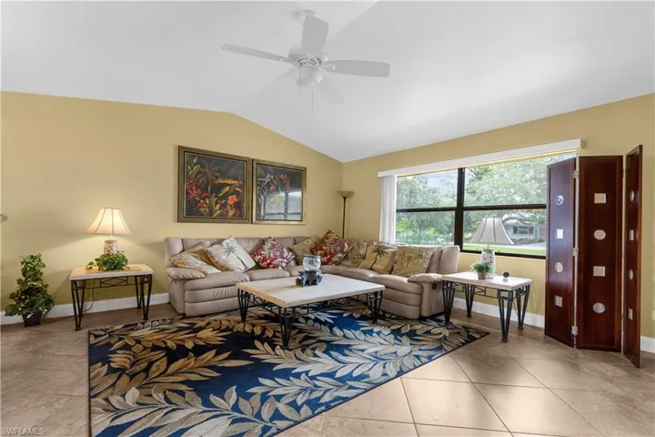 Living room featuring vaulted ceiling, ceiling fan, and light tile patterned floors