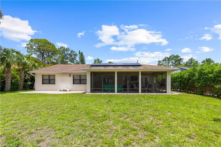 Back of house with a sunroom, solar panels, a lawn, stucco siding, and a patio area