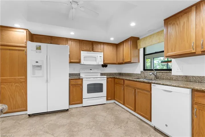 Kitchen featuring white appliances, brown cabinets, a ceiling fan, recessed lighting, and dark stone counters