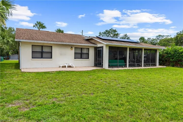 Back of house featuring a sunroom, a yard, stucco siding, roof mounted solar panels, and a patio
