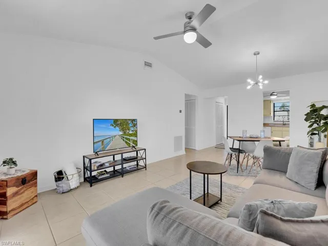 Tiled living room featuring ceiling fan with notable chandelier, sink, and vaulted ceiling