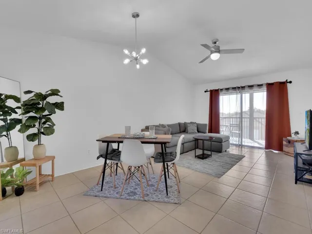 Dining space with light tile patterned floors, ceiling fan with notable chandelier, and high vaulted ceiling