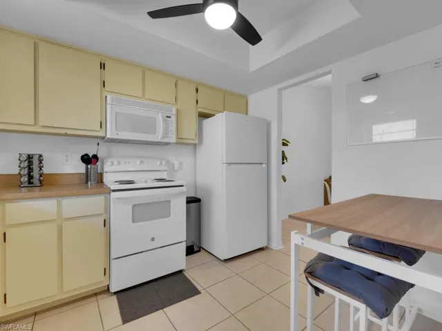 Kitchen with ceiling fan, light tile patterned flooring, white appliances, and cream cabinets