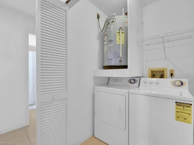 Laundry area featuring light tile patterned floors, electric water heater, and separate washer and dryer