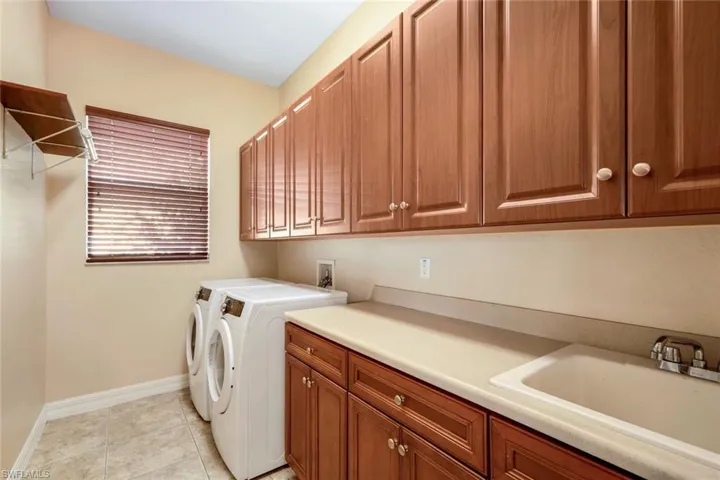 Large laundry room with appliances, lots of cabinets, big sink, countertop folding space and hanging rack.