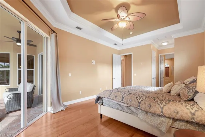 Primary Bedroom with access to lanai/pool, crown molding, decorative ceiling fan, light wood-type flooring, and a tray ceiling.