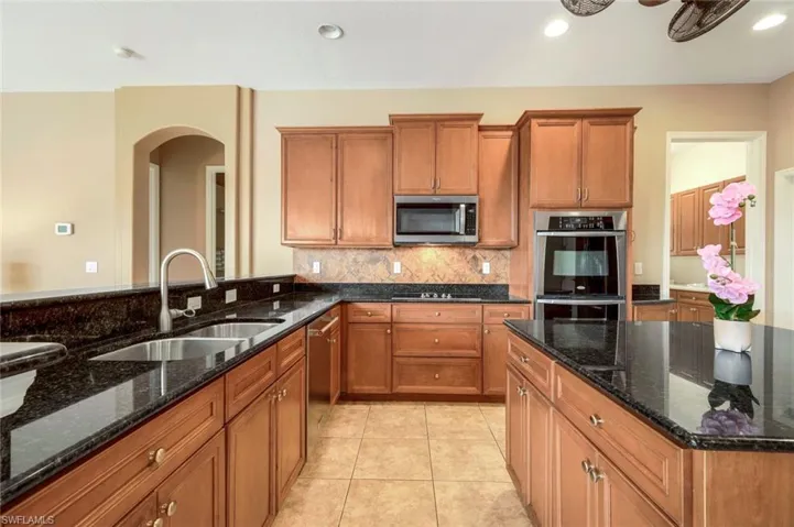 Large Kitchen featuring decorative backsplash, dark stone countertops, big center island, appliances with stainless steel finishes, and light tile patterned flooring.