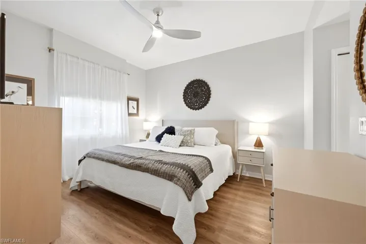 Neutral interior featuring wood-finish flooring, a modern three-blade ceiling fan with integrated lighting, and a window with neutral drapery hardware