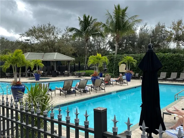 Clubhouse swimming pool featuring a paver stone deck, perimeter metal fencing, and an integrated pavilion
