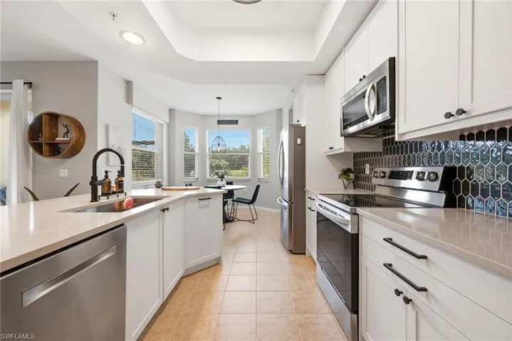 Kitchen featuring white shaker-style cabinetry, quartz countertops, a black geometric tile backsplash, stainless steel appliances, and a recessed tray ceiling