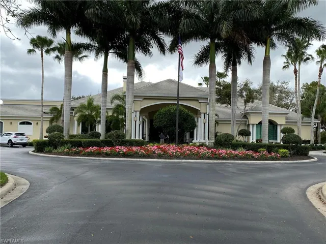 Clubhouse Exterior facade featuring a covered portico with columns, mature palm trees, a circular driveway, and manicured landscaping