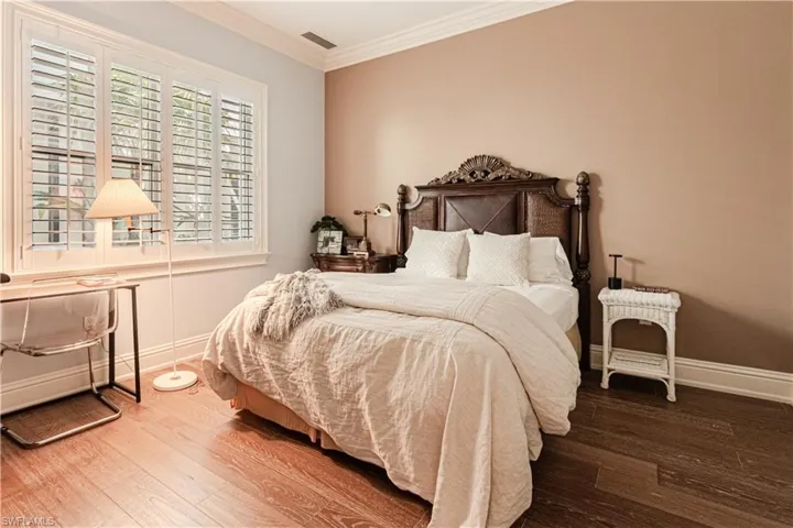 Bedroom with baseboards, wood finished floors, visible vents, and crown molding