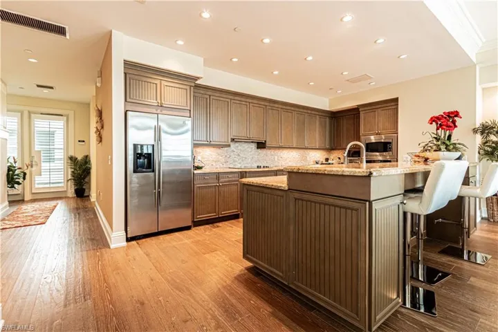 Kitchen featuring light stone counters, light wood-style flooring, visible vents, appliances with stainless steel finishes, and decorative backsplash