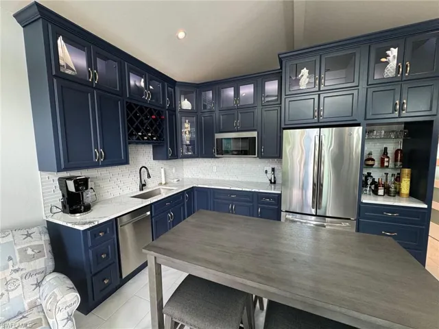 Kitchen with backsplash, light tile patterned floors, stainless steel appliances, sink, and blue cabinets