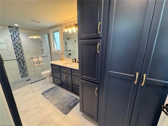 Bathroom featuring toilet, a tile shower, and vanity