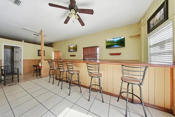 Indoor dry bar featuring a ceiling fan, light tile patterned floors, a wainscoted wall, and wooden counters