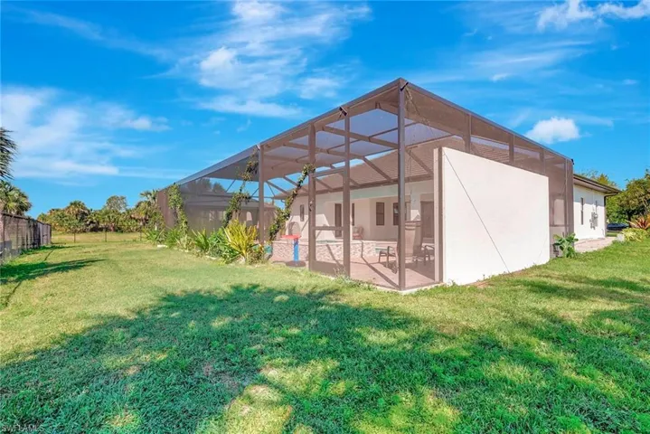 Back of house featuring glass enclosure, a patio area, and a lawn