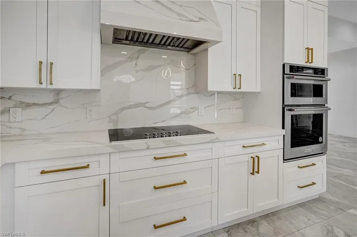 Kitchen with light stone counters, stainless steel double oven, extractor fan, white cabinets, and black electric stovetop