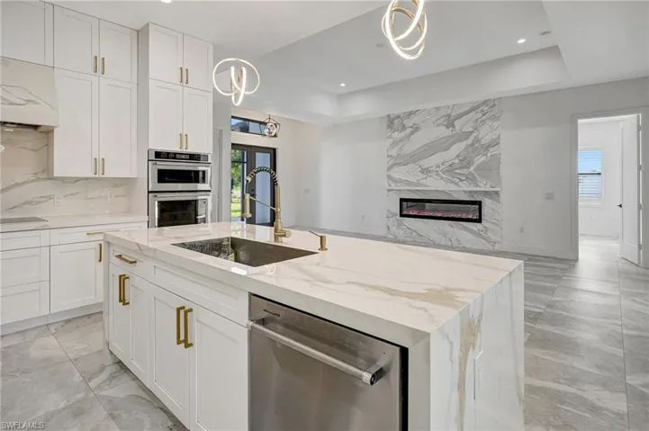 Kitchen with a premium fireplace, a sink, decorative backsplash, stainless steel appliances, and white cabinets