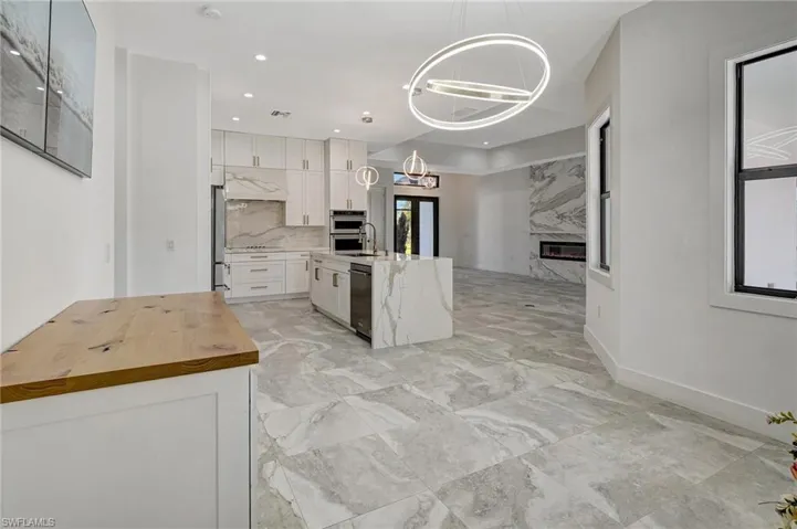Kitchen featuring wooden counters, a premium fireplace, white cabinets, under cabinet range hood, and a notable chandelier