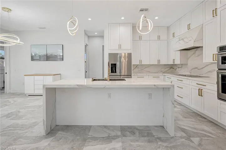 Kitchen featuring visible vents, a kitchen island with sink, under cabinet range hood, backsplash, and appliances with stainless steel finishes