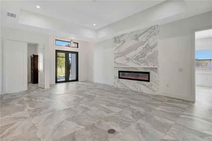 Unfurnished living room with baseboards, a premium fireplace, recessed lighting, french doors, and a raised ceiling
