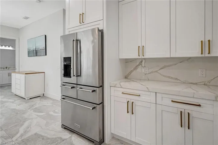 Kitchen featuring light stone counters, visible vents, stainless steel refrigerator with ice dispenser, marble finish floor, and backsplash