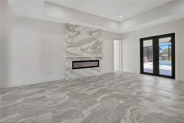 Unfurnished living room with a raised ceiling, french doors, baseboards, and a high end fireplace